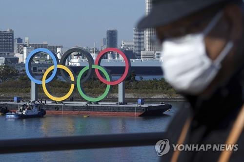 지난달 1일 일본 도쿄도(東京都)에서 마스크를 쓴 남성이 이동하는 가운데 오다이바 해변 공원에 도쿄올림픽을 상징하는 조형물이 보인다. 신종 코로나바이러스 감염증(코로나19)이 급격하게 확산하면서 도쿄 올림픽·패럴림픽 개최가 어렵다는 관측이 대두하고 있다.